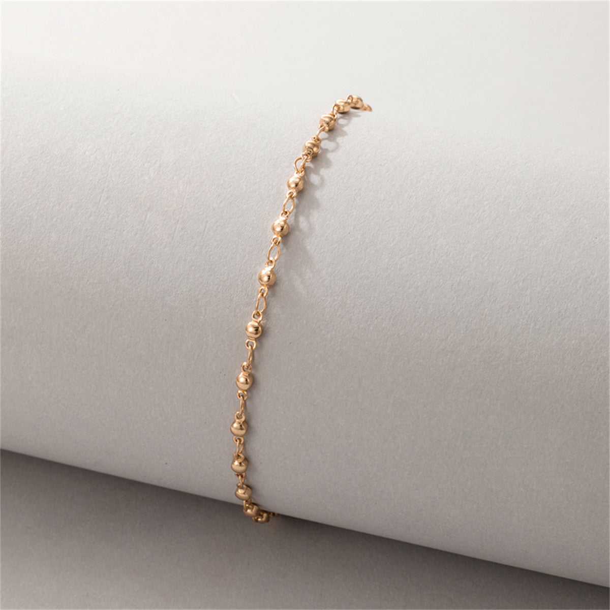 Chic 18K gold-plated beaded chain anklet showcased on a white surface, reflecting its stylish and luxurious appeal.