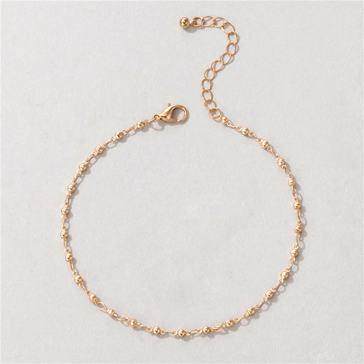 Dazzling 18K gold-plated beaded chain anklet on a white surface, capturing its elegance and sophisticated charm.