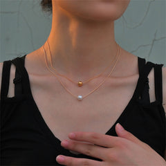 A layered necklace featuring two gold and white pearls, complemented by 18K gold-plated beads.