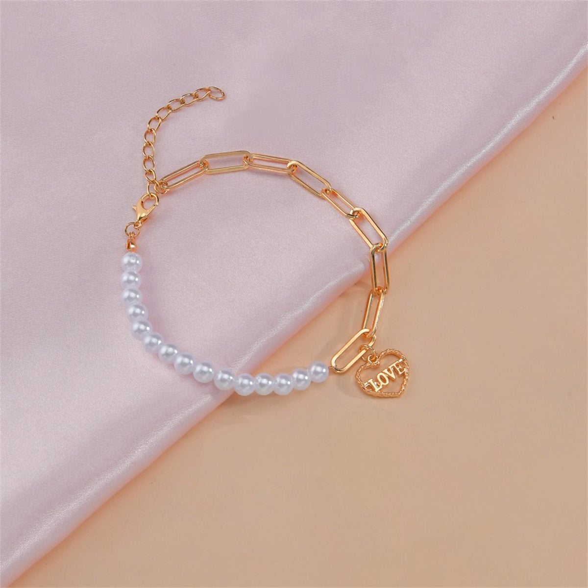 A refined bracelet of white pearls with a gold heart charm, symbolizing love and grace in a timeless design.