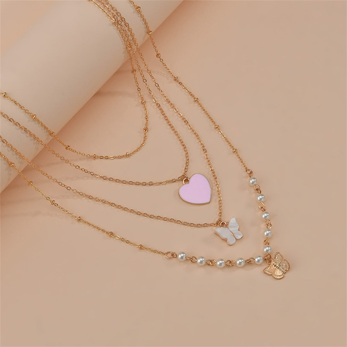 A layered necklace showcasing a pink heart pendant, butterfly charm, and pearls, all in 18K gold plating.