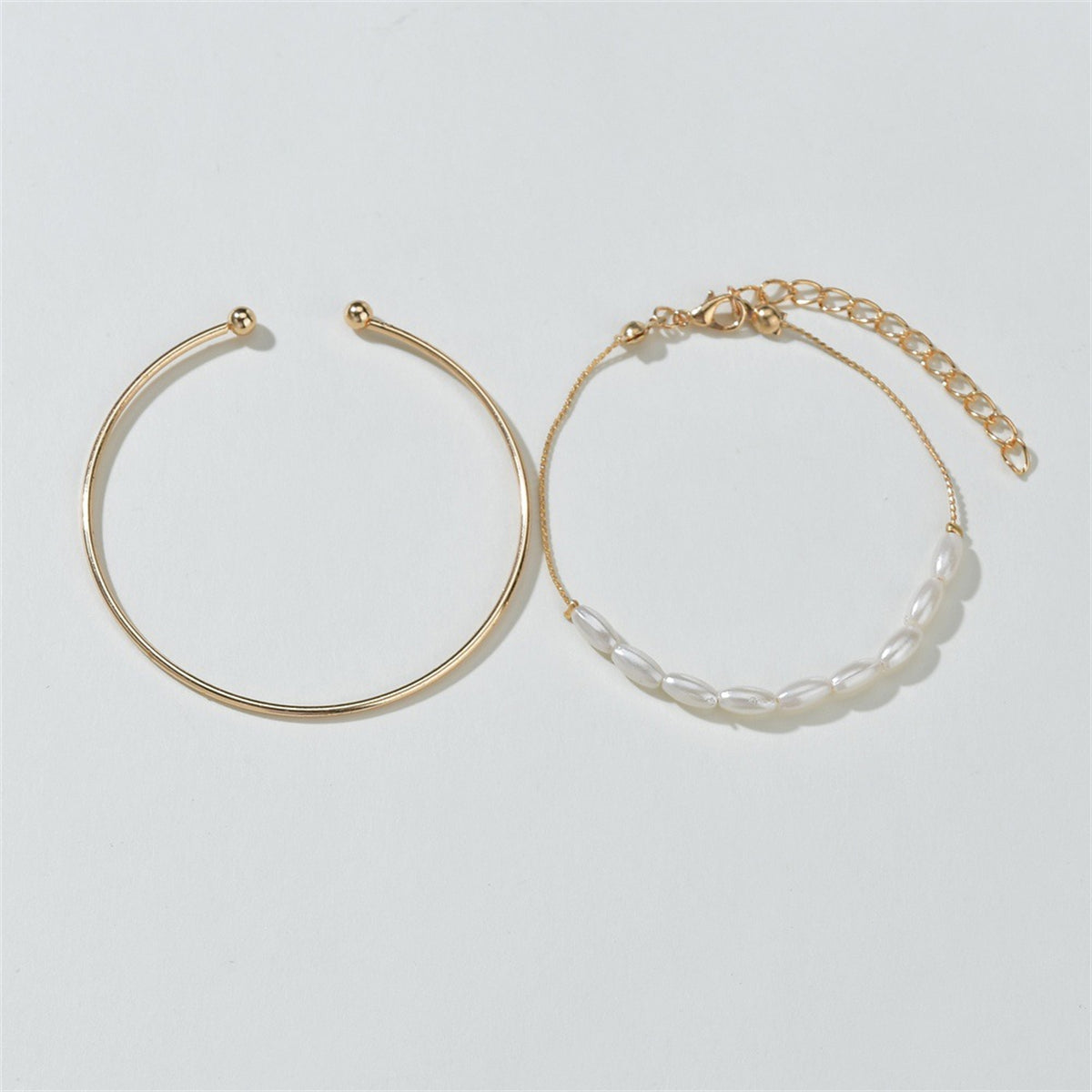 Two exquisite gold bangles with pearls and a chain, highlighting the beauty of the Pearl & 18K Gold-Plated Oval Bracelet Set.