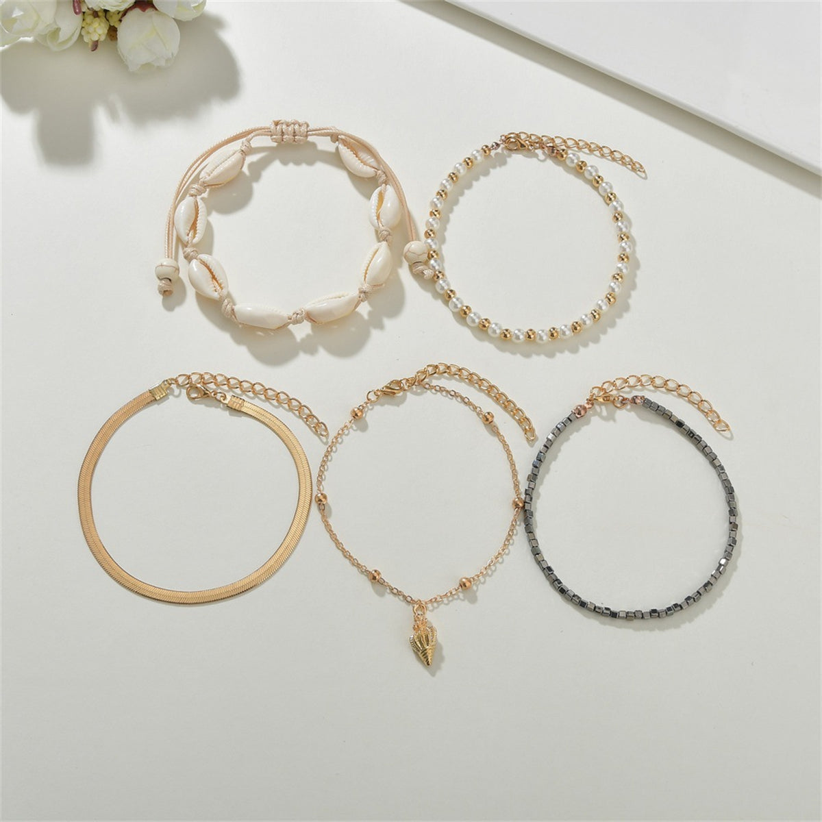 Three stylish gold and black anklets embellished with shells and pearls, part of a refined 18K gold-plated anklet set.