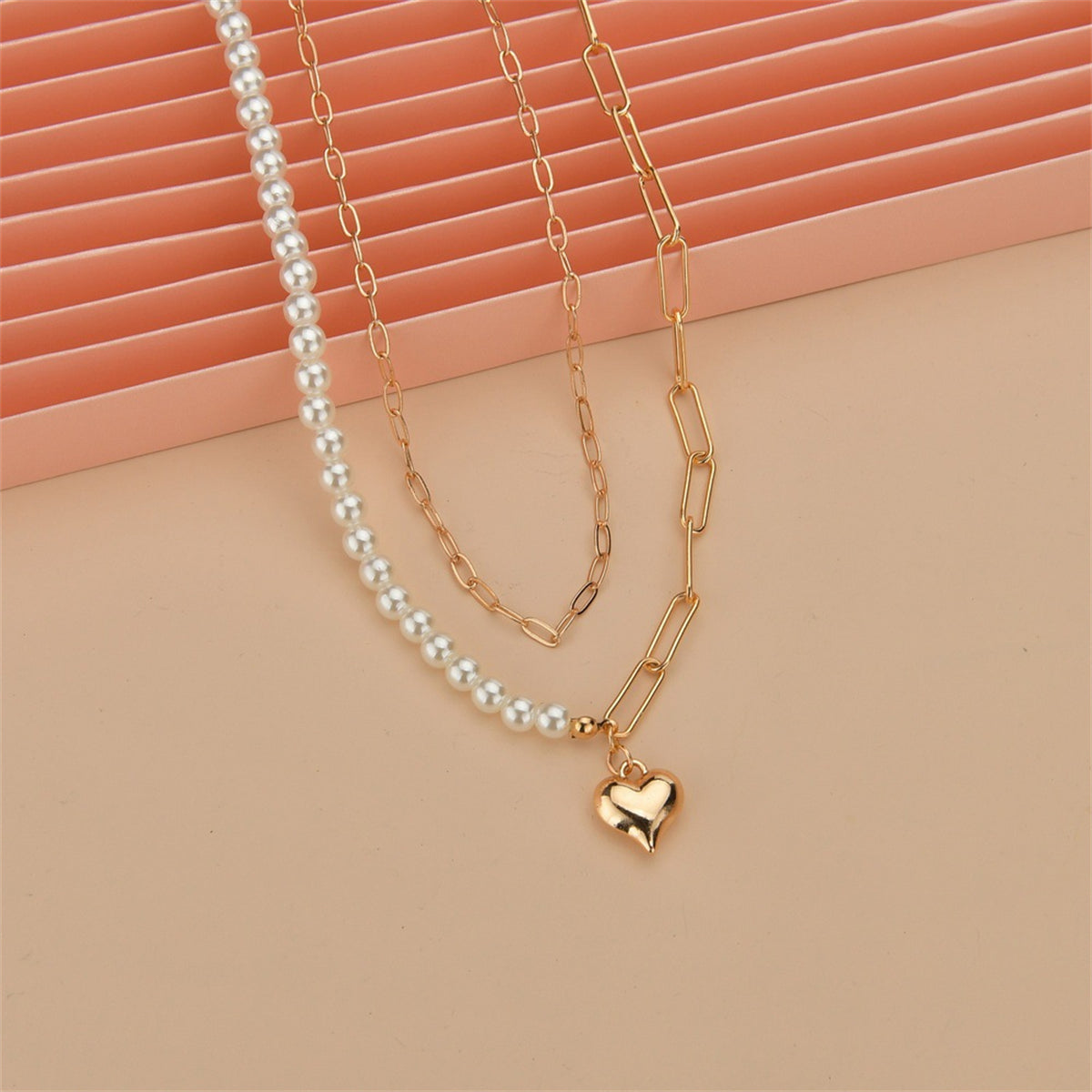 An elegant gold chain necklace with a heart charm and a pearl, beautifully layered for a stylish accessory.