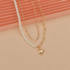 An elegant gold chain necklace with a heart charm and a pearl, beautifully layered for a stylish accessory.