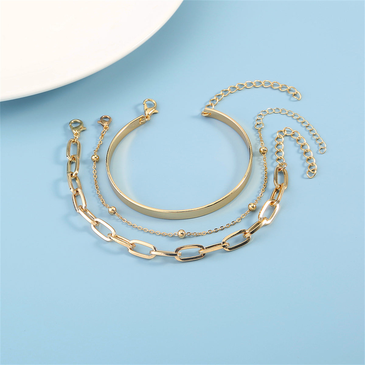 Two beautiful gold chains and a bracelet resting on a white surface, showcasing the refined 18K gold-plated bead and cable design.