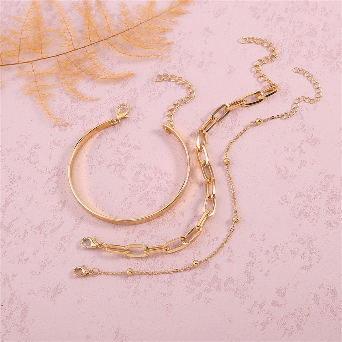 Two luxurious gold chains alongside a chic bracelet on a white surface, highlighting the exquisite 18K gold-plated craftsmanship.